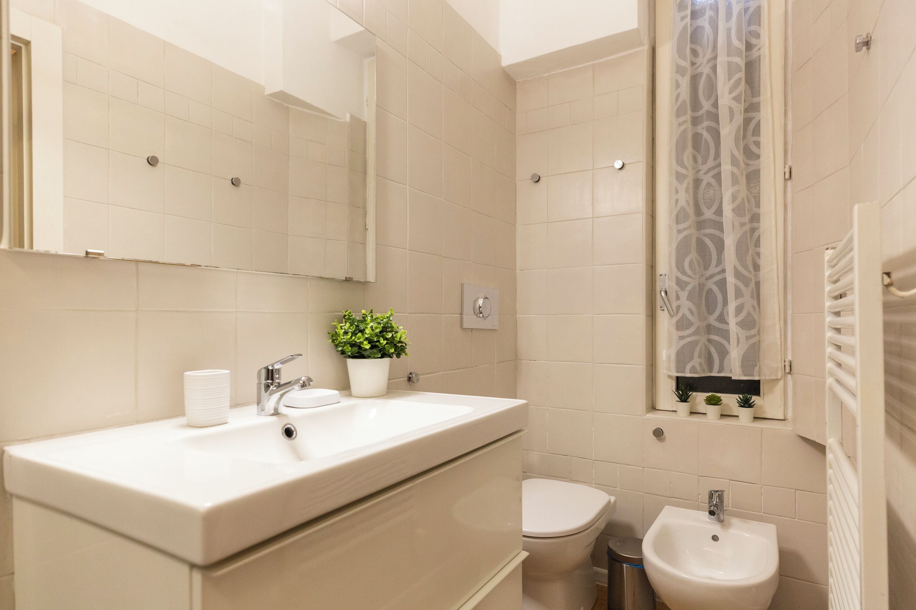 A modern bathroom with a large mirror, a sink, a toilet, and a bidet.