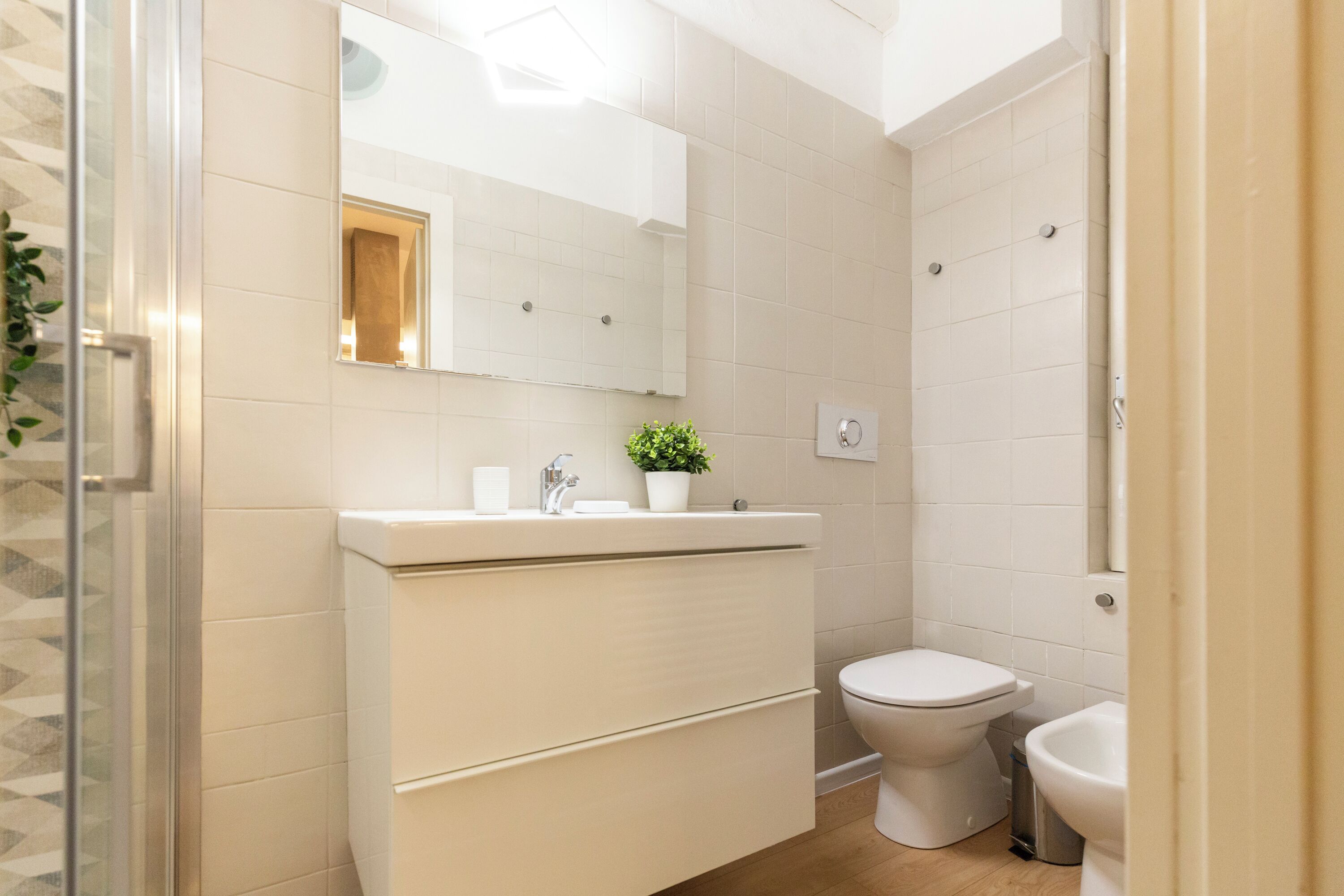 A modern bathroom with a glass shower enclosure, a white sink with a mirror above it, a toilet, and a bidet.