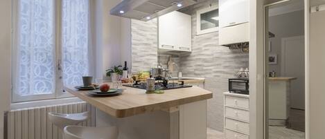 A modern kitchen with a central island, white cabinetry, and a window with patterned curtains.