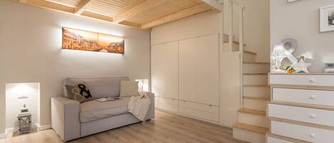 Una sala de estar moderna con techo de madera, un sofá gris, un aparador blanco y una escalera.