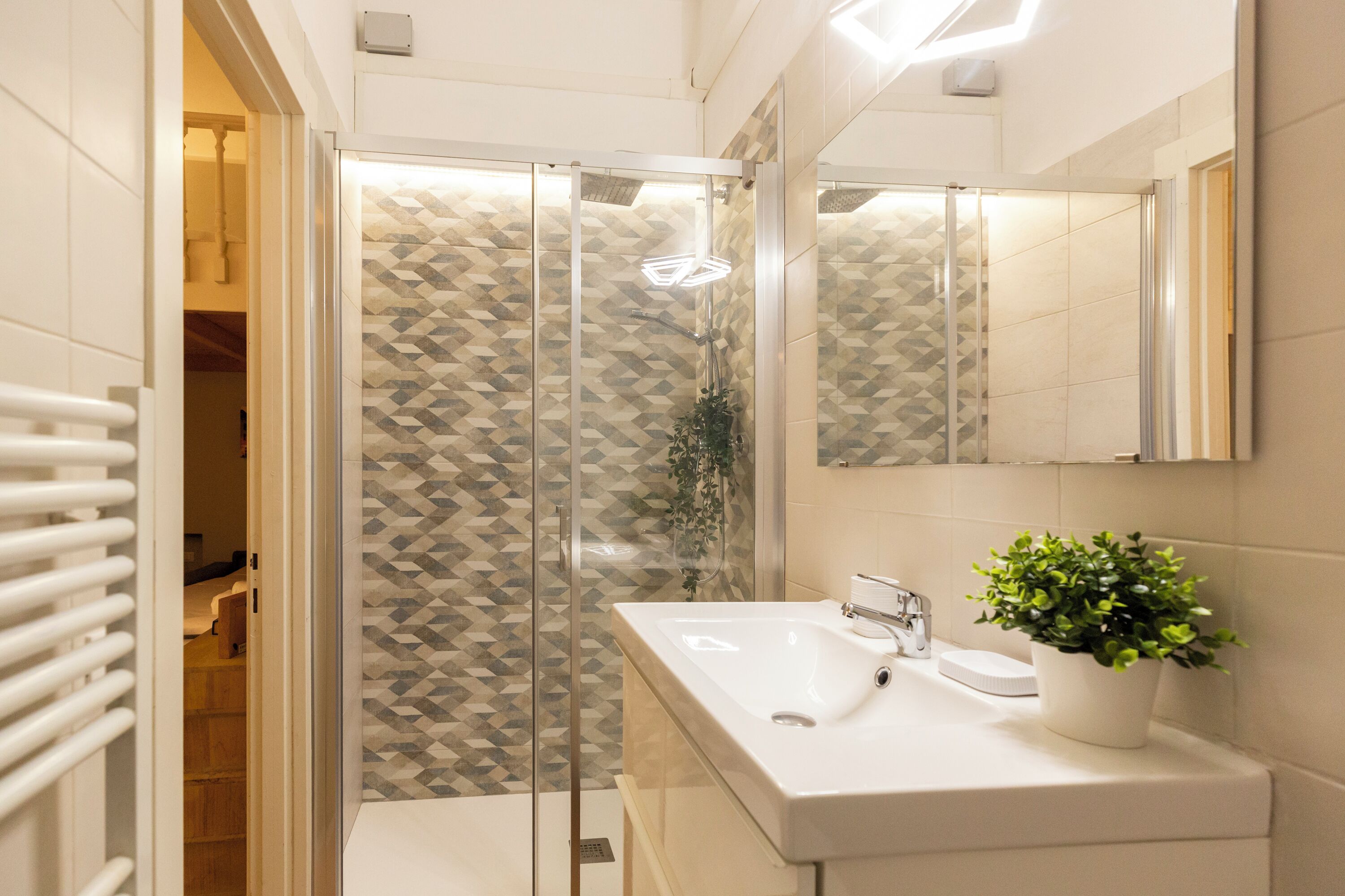 A modern bathroom with a glass shower enclosure, a white sink, and a potted plant.