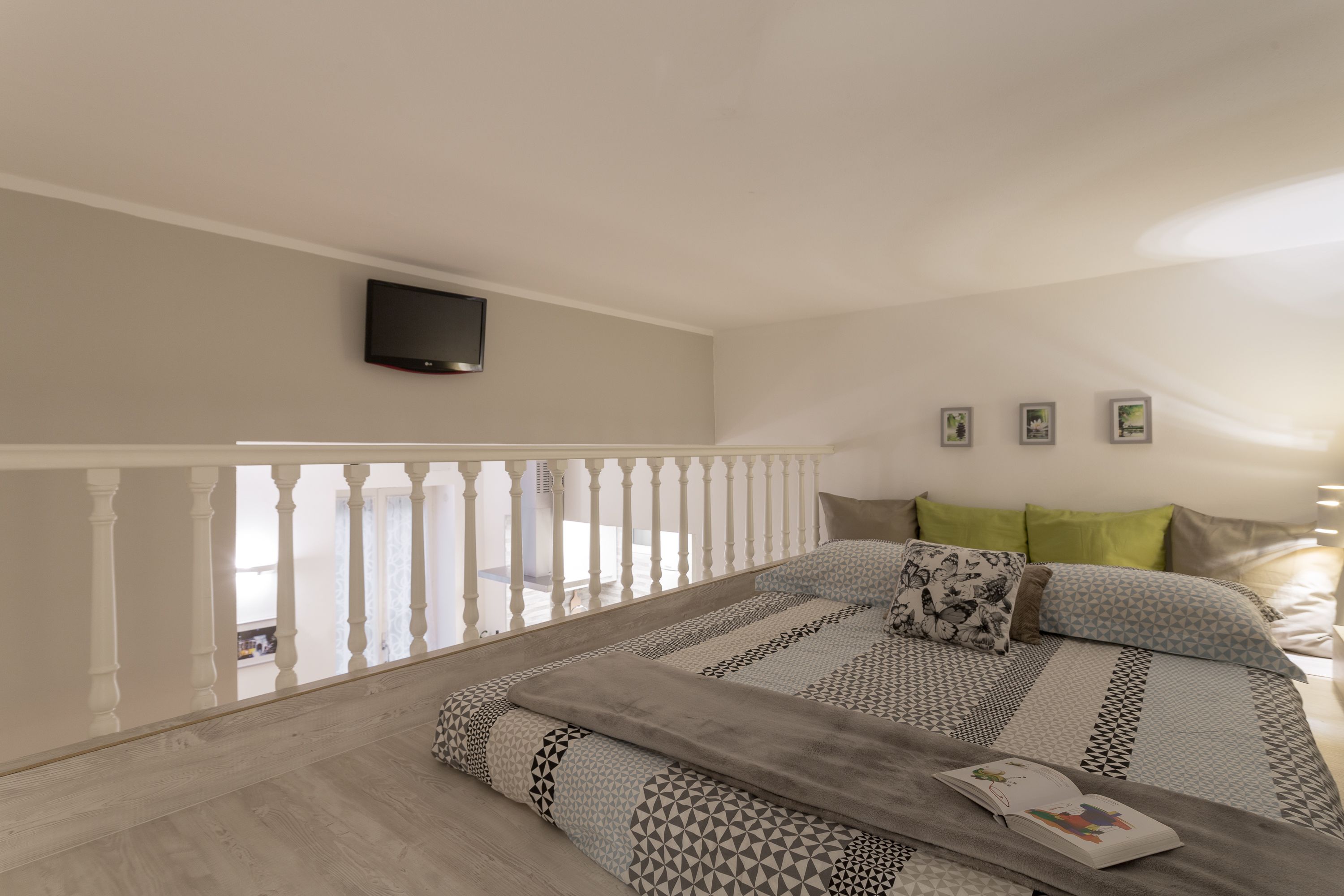 A bedroom with a bed, a TV mounted on the wall, and a balcony with a railing.