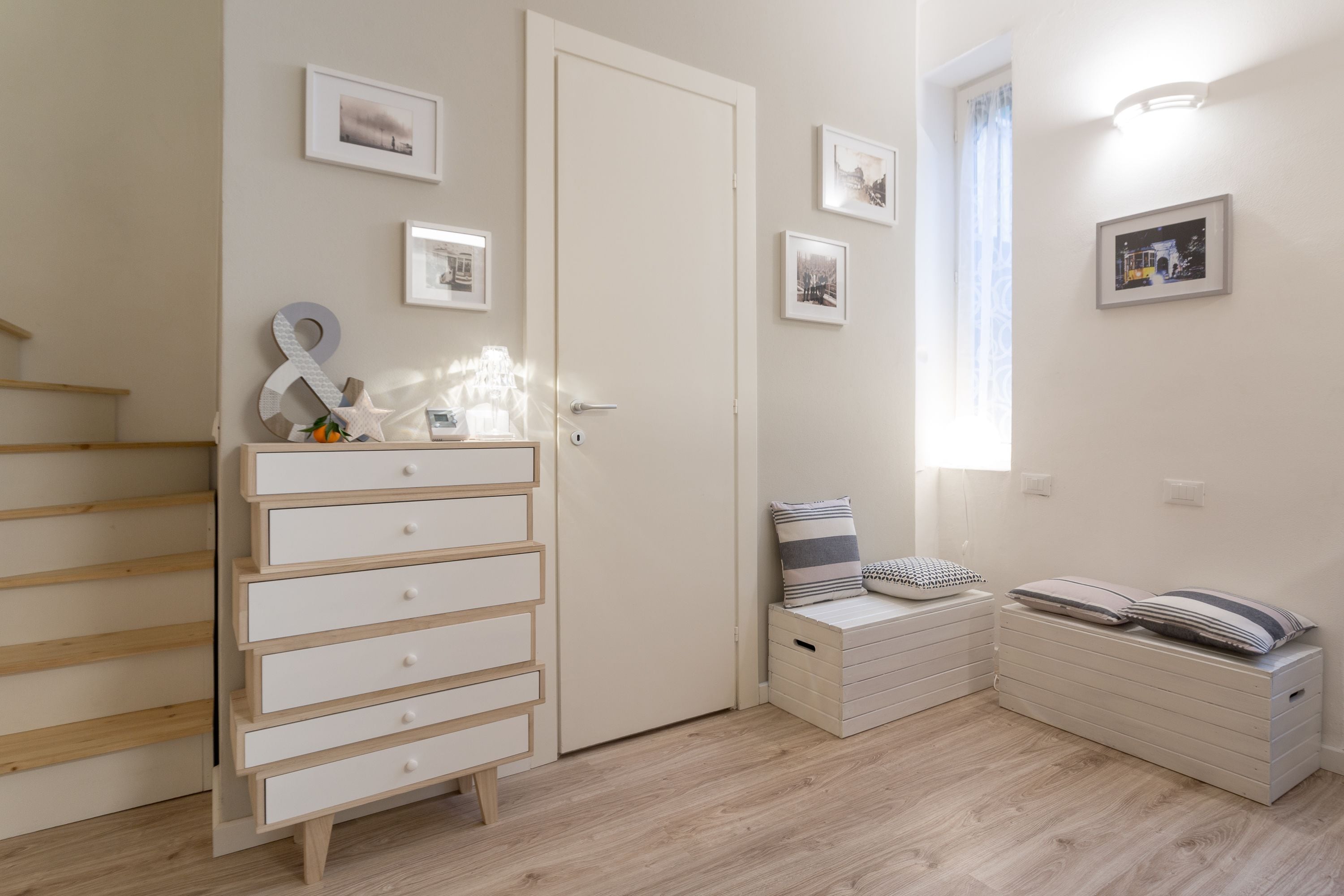 Un dormitorio con piso de madera, un aparador blanco, una cama con almohadas y un ventanal con cortinas.