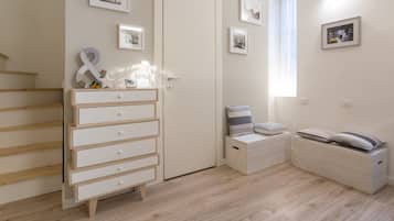 Un dormitorio con piso de madera, un aparador blanco, una cama con almohadas y un ventanal con cortinas.