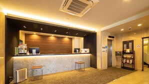 Zona de recepció d'hotel amb un taulell de marbre, dos tamborets, un ordinador d'escriptori i un aire condicionat fixat a la paret.