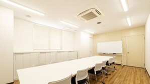 Una sala de conferències amb una taula llarga, cadires blanques, una pissarra i una finestra amb persianes.