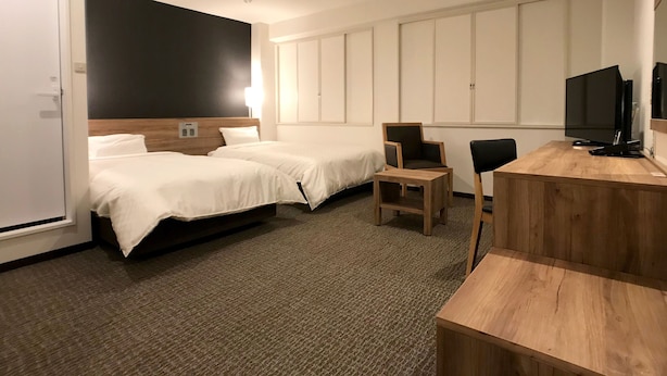 Habitació d'hotel amb dos llits, un escriptori, una cadira, una televisió i un armari.