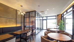 Interior modern d'un restaurant amb una taula de fusta llarga, cadires amb coixins i un gran finestral que ofereix vistes a l'exterior.