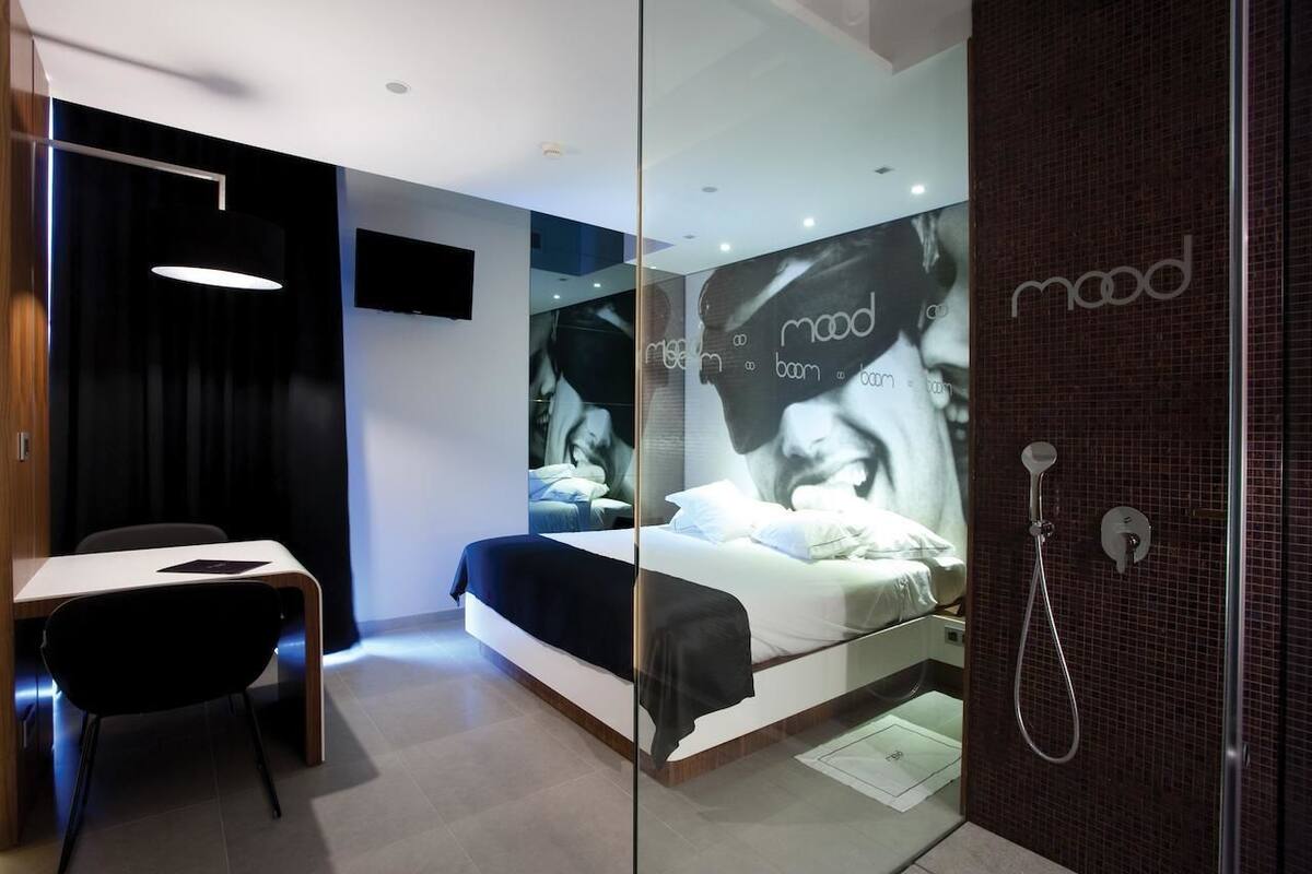 A modern hotel room with a bed, a desk, and a shower.