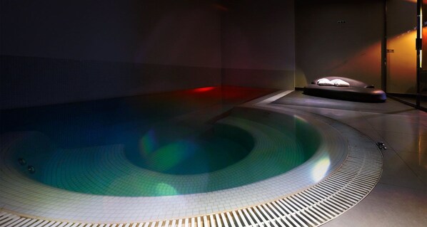 A modern indoor pool with a circular design and a seating area with a light source. - Mood - Private Suites (Montijo)