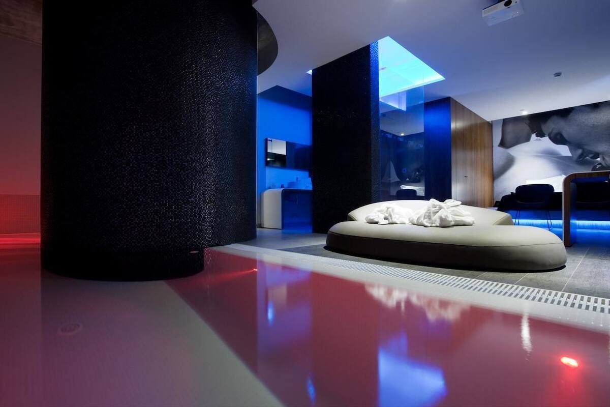 A modern spa room with a large black column, a white massage table, and a blue-lit ceiling.