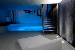 A modern hotel room with a blue-lit pool, a staircase, and a textured wall. - Mood - Private Suites (Montijo)