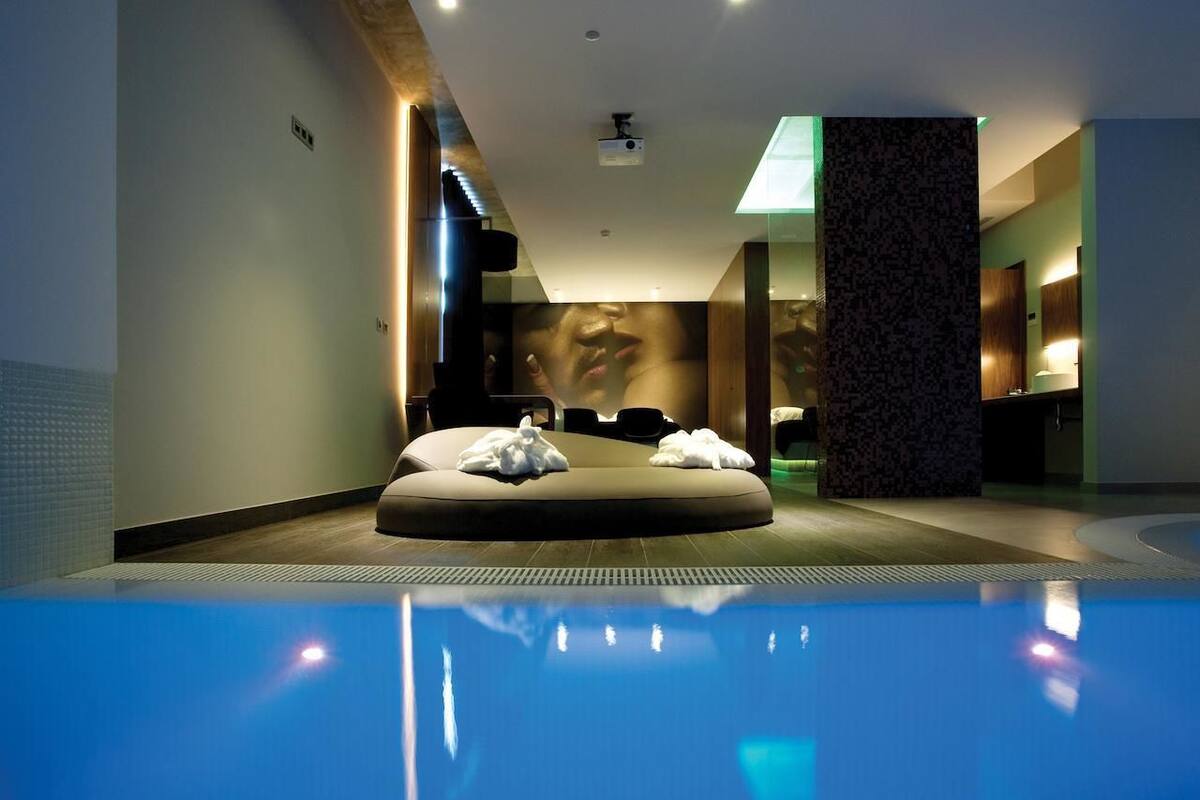 A modern spa room with a pool, a massage chair, and a large mirror.