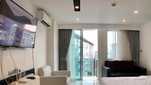 A modern hotel room with a bed, a sofa, a TV, and a balcony with a city view. - City Center Residence by PSR ASIA (Pattaya)