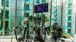 A fitness area with cardio machines and a sign reading "DISCO SONGS" in a modern building with large windows. - City Center Residence by PSR ASIA (Pattaya)