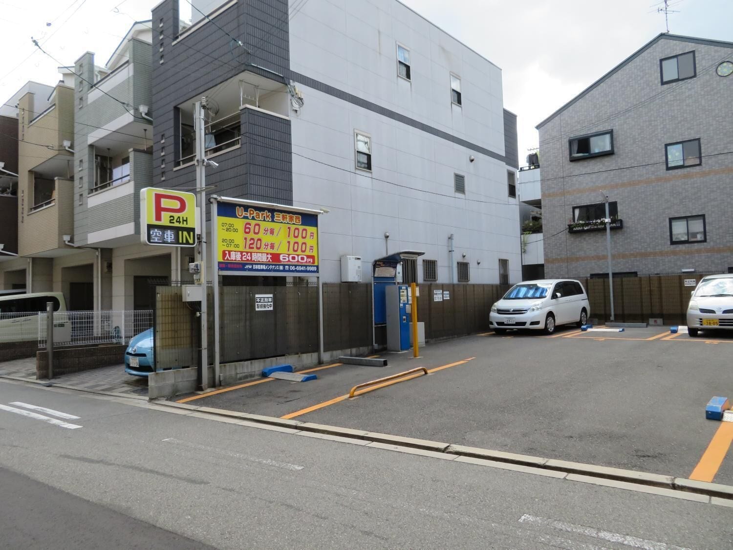 A parking lot with a sign indicating a 24-hour parking rate of 100 yen per hour.