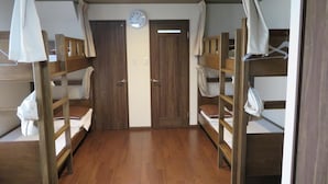 A dormitory room with bunk beds, a wooden floor, a clock on the wall, and a door with a curtain. - Azalea - Hostel (Osaka)