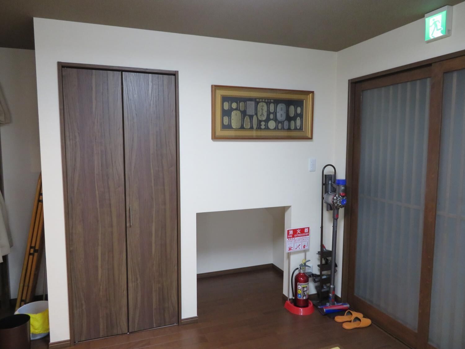 A hallway with a wooden wardrobe, a framed picture on the wall, and a fire extinguisher on the right.