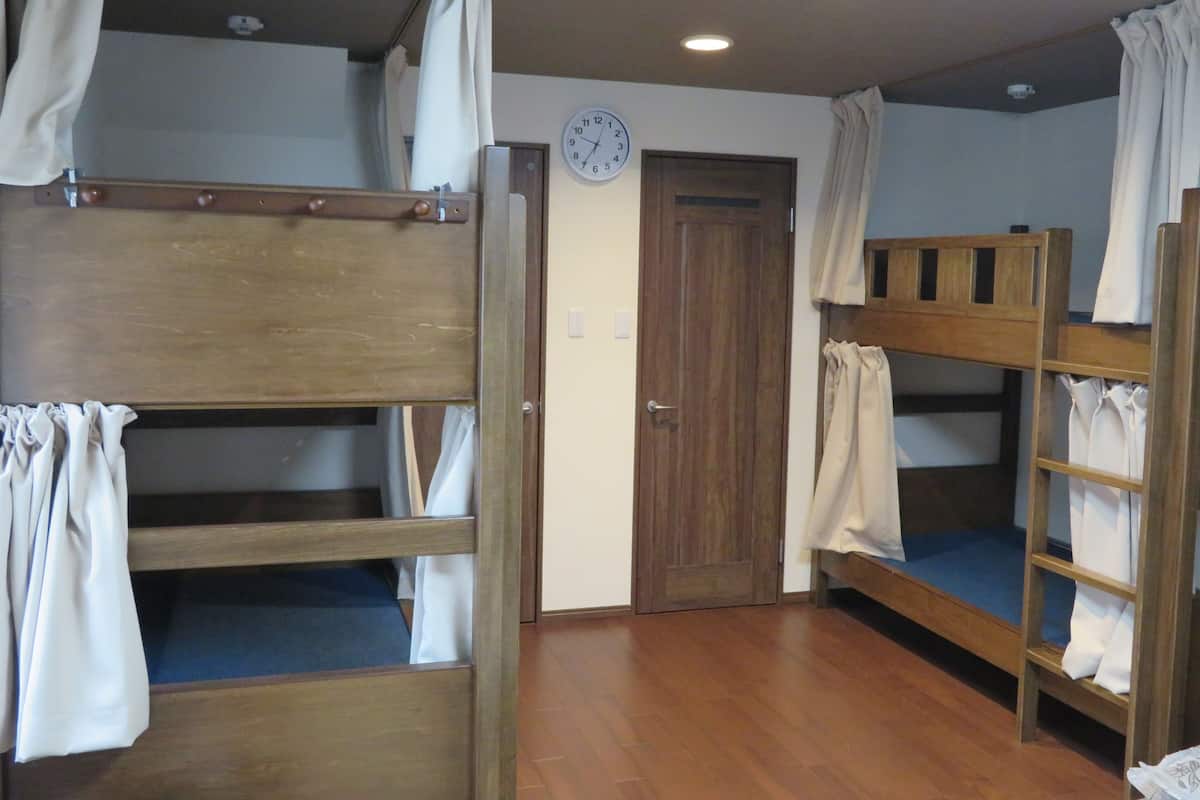 A room with bunk beds, a wooden door, a clock on the wall, and a ceiling light.