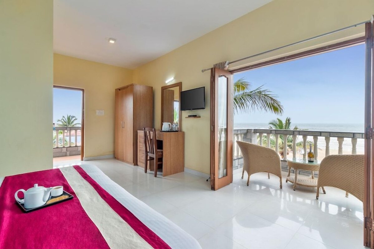 Quarto de hotel com cama, escrivaninha, televisão e varanda com mobiliário de vime.