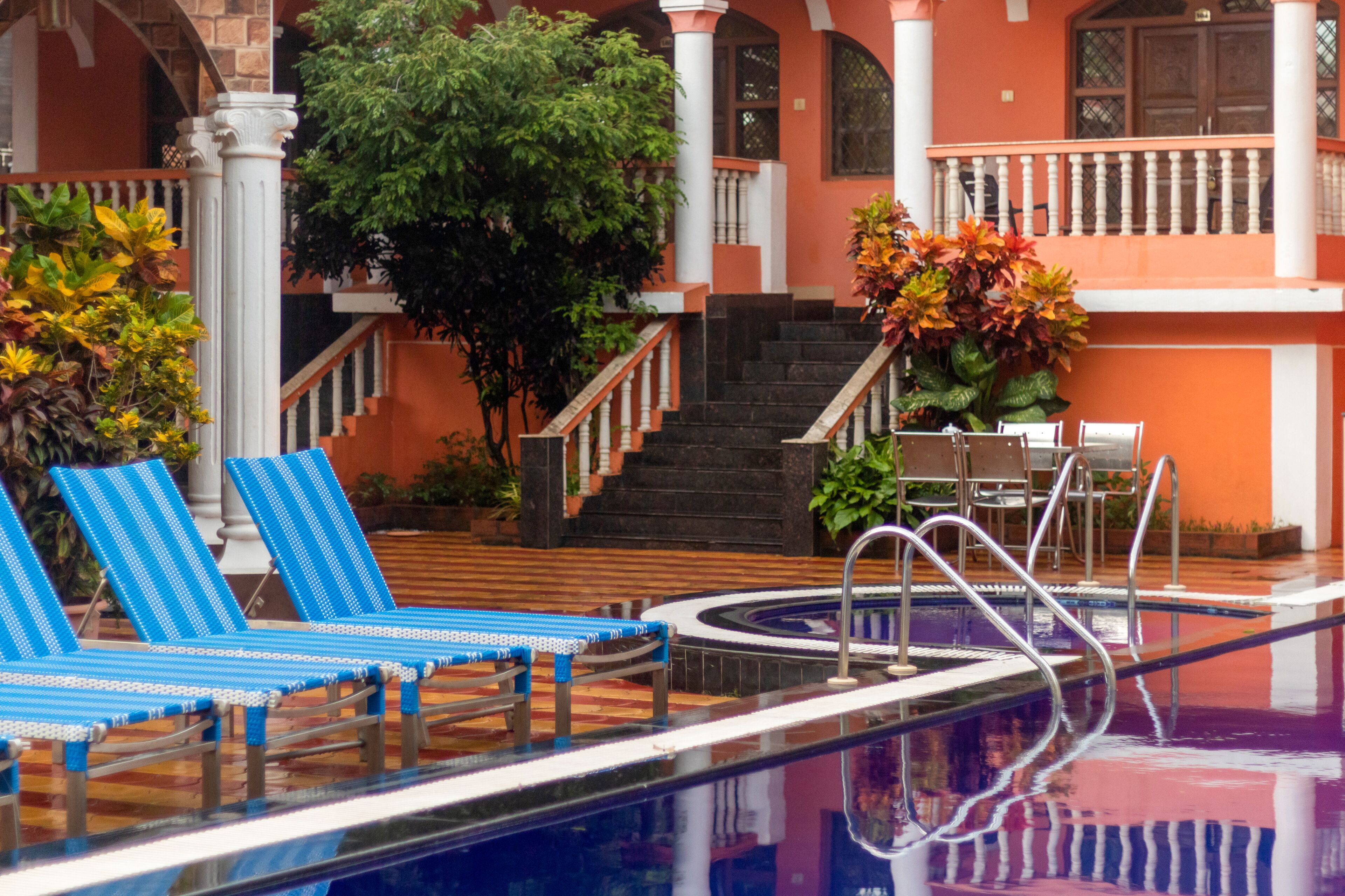 Piscina con sillas reclinables azules, una escalera y un balcón con paredes naranja y barandillas blancas.