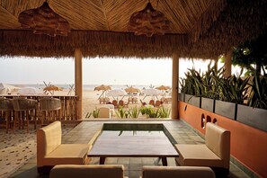 A beachside lounge with a thatched roof, outdoor seating, and a view of the beach. - Larios Beach Holidays (Baga)