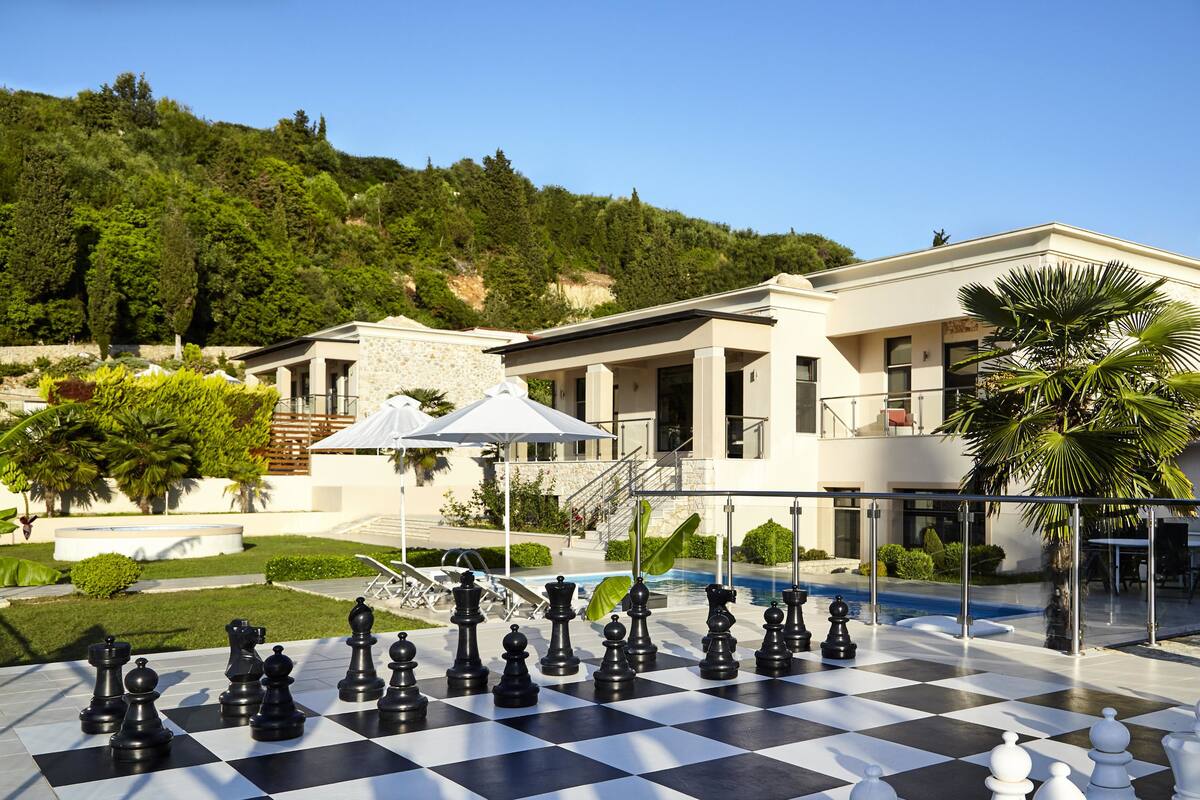 A large outdoor chessboard set up in a courtyard with a pool and a modern building in the background.
