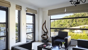 Ein modernes Wohnzimmer mit einer schwarzen Couch, einem Couchtisch und einem großen Fenster mit Blick auf eine grüne Landschaft.