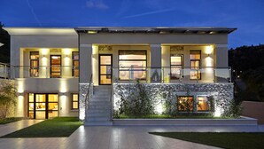 Ein modernes, zweistöckiges Haus mit Natursteinfassade, großen Fenstern und einer hell erleuchteten Eingangspartei.