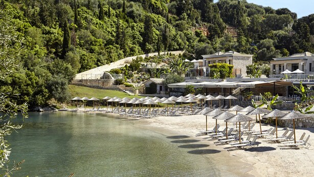 Ein Strandresort mit Liegestühlen und Sonnenschirmen, einem Pool und Gebäuden mit steinernen Fassaden.