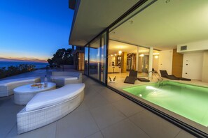 A modern outdoor pool area with glass walls, lounge chairs, and a dining setup. - Golden Rays Luxury Villas (Primosten)