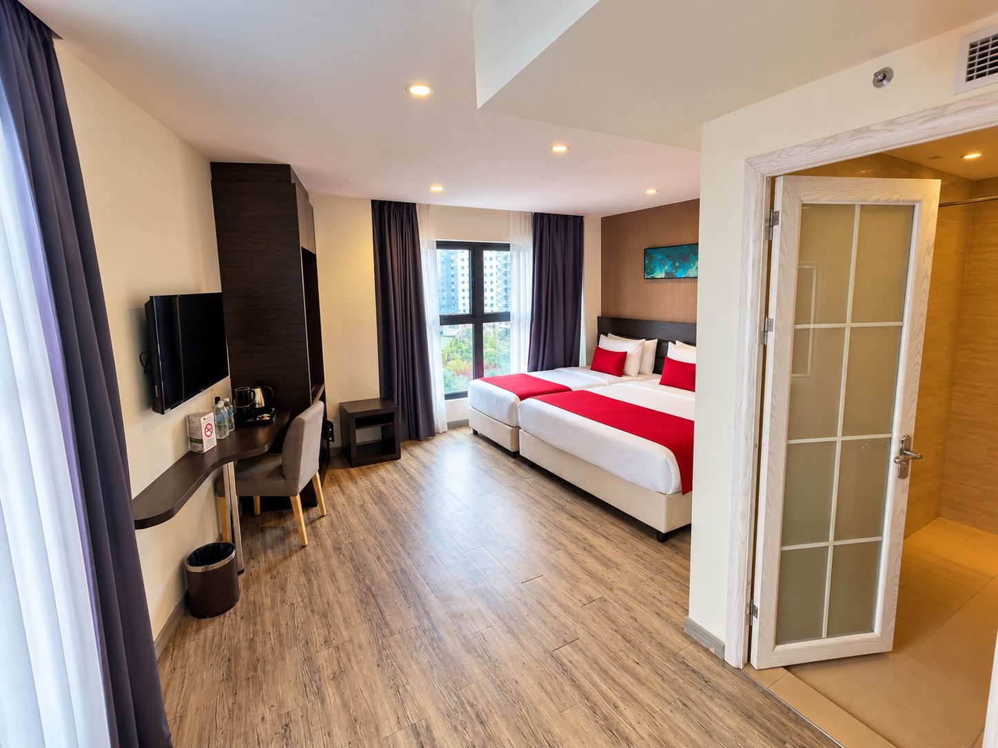 Habitación de hotel con cama, escritorio, televisor y vistas al exterior.