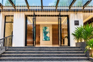 Entrada de hotel con fachada de vidrio, una escalera que lleva al vestíbulo y un cuadro abstracto de gran tamaño.