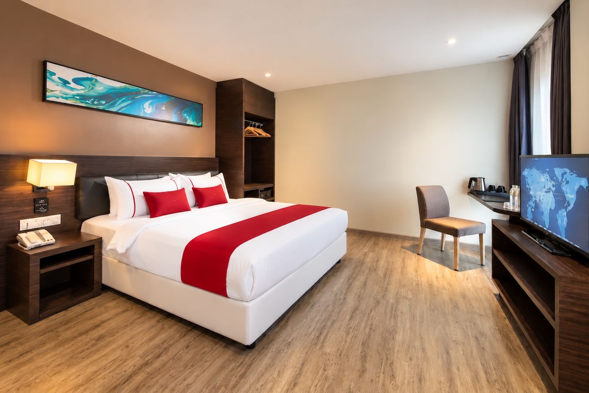 Een hotelkamer met een bed, nachtkastje, lamp, televisie en een schilderij aan de muur.