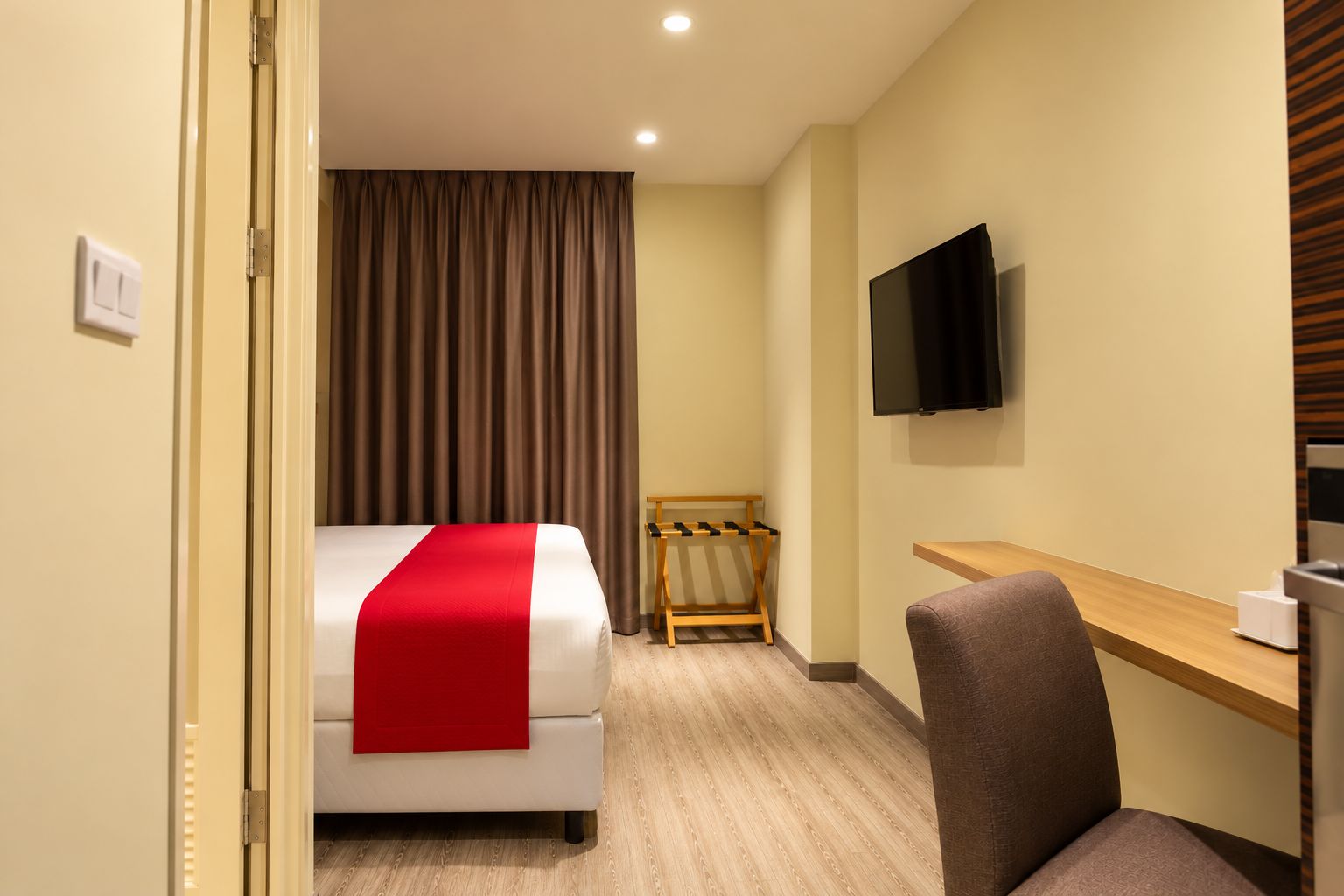 A hotel room with a bed, a desk, a chair, a TV, and a coat rack.