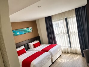 Une chambre d’hôtel avec deux lits, une grande fenêtre avec des rideaux, un tableau au mur et une chaise.