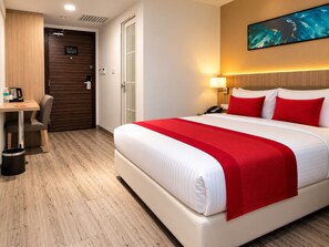 Une chambre d’hôtel comprenant un lit, un bureau, une chaise, une poubelle, une porte et un tableau accroché au mur.
