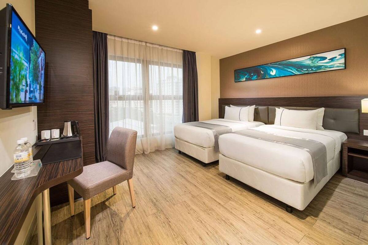 A hotel room with two beds, a desk with a chair, a TV, and a window with curtains.