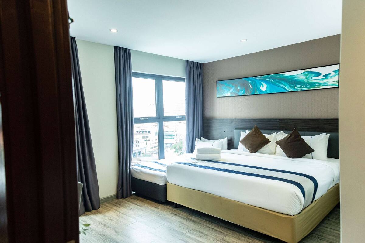 A hotel room with a large bed, a window with curtains, a painting on the wall, and a view of the city.