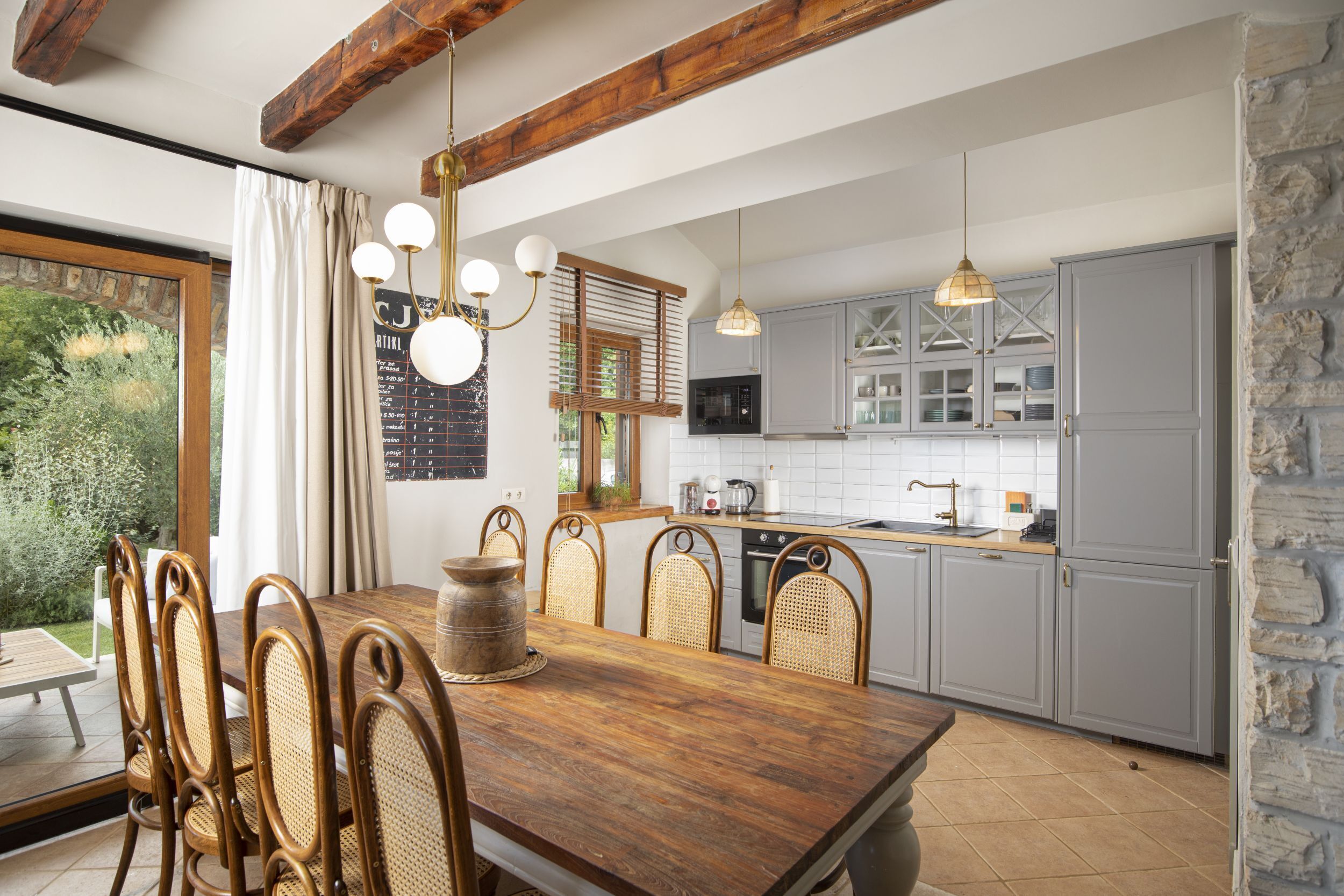 Une cuisine moderne avec des meubles de couleur grise, une table à manger en bois, des chaises en osier et des luminaires suspendus.