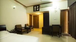A hotel room with a bed, two chairs, a small table, a desk, and an air conditioning unit. - White Orchid (Cox's Bazar)