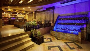 A hotel lobby with a stone wall water feature, a reception desk, and a staircase leading to the upper floor. - White Orchid (Cox's Bazar)