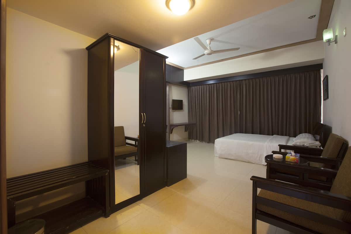 A hotel room with a bed, a desk, a chair, a wardrobe, and a ceiling fan.