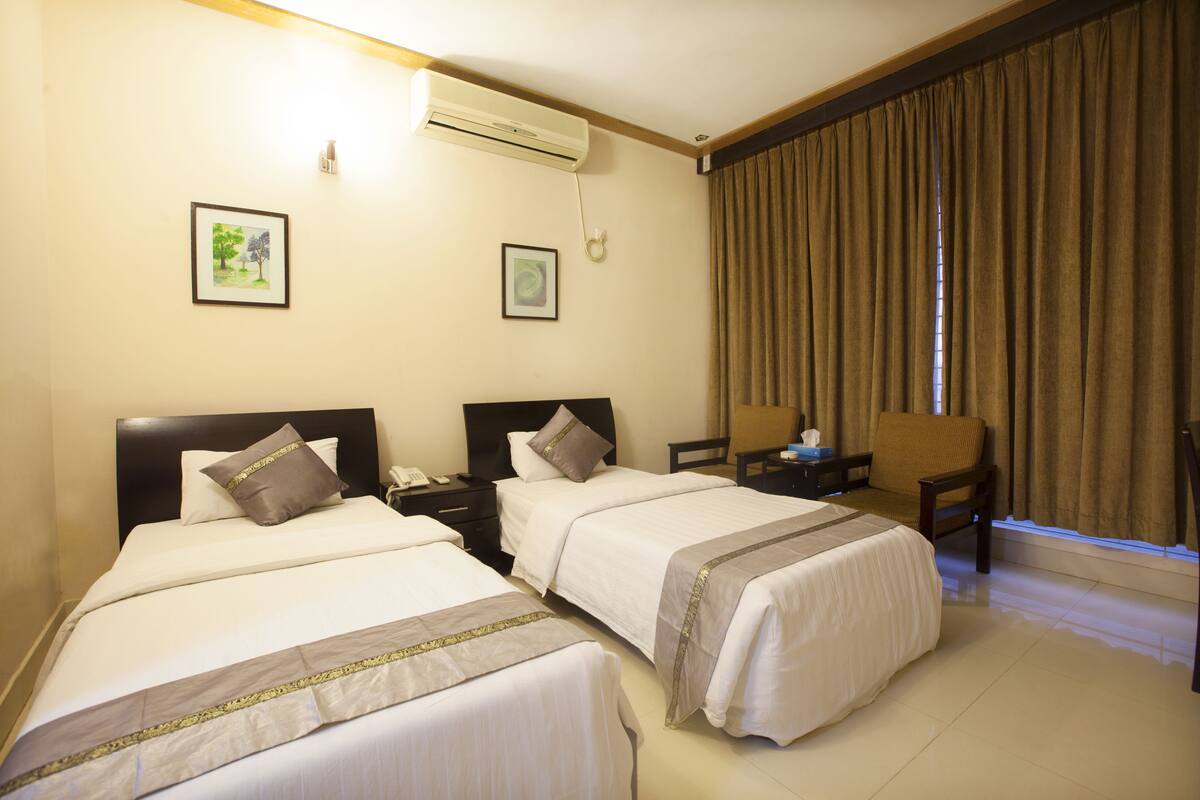 A hotel room with two beds, a nightstand, a chair, and a window with curtains.