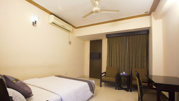 A hotel room with a bed, a desk, a chair, a ceiling fan, an air conditioning unit, and a television. - White Orchid (Cox's Bazar)