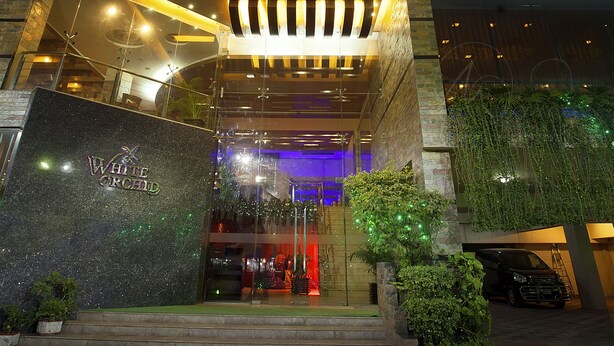 A hotel entrance with a glass facade, a stone wall with the name "WHITE ORCHID," and a staircase leading up to the entrance. - White Orchid (Cox's Bazar)
