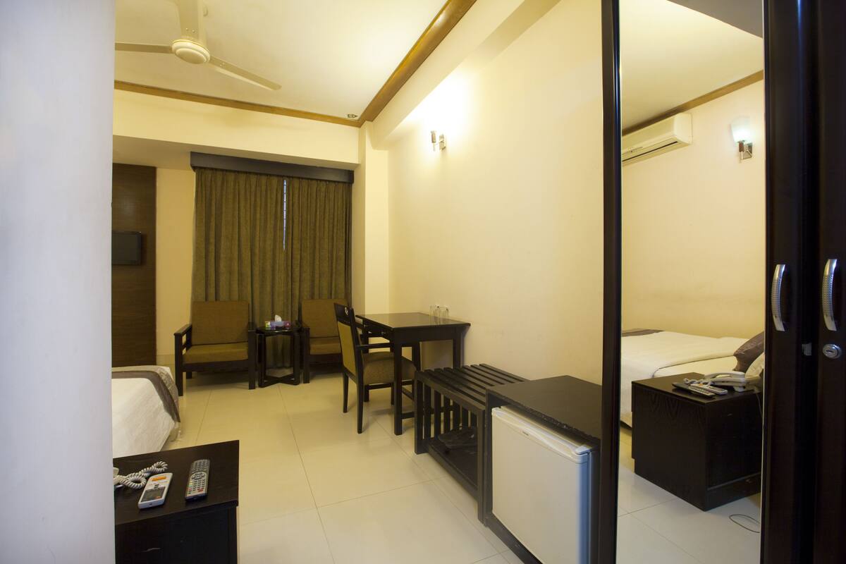 A hotel room with a bed, a desk with a chair, a small table with a phone, a radiator, and a TV on the wall.