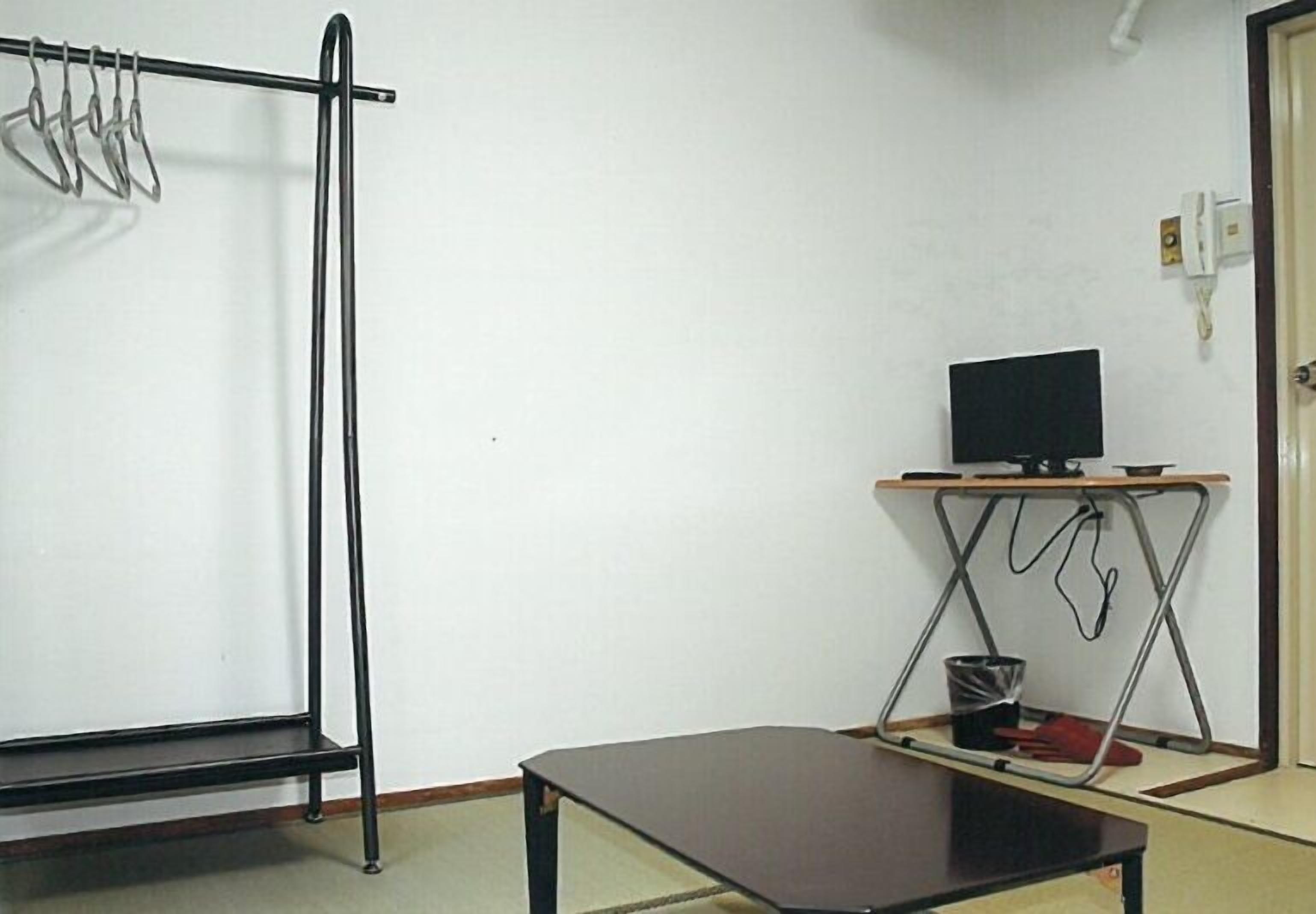 A room with a bed, a small table, a television on a stand, and a coat rack.