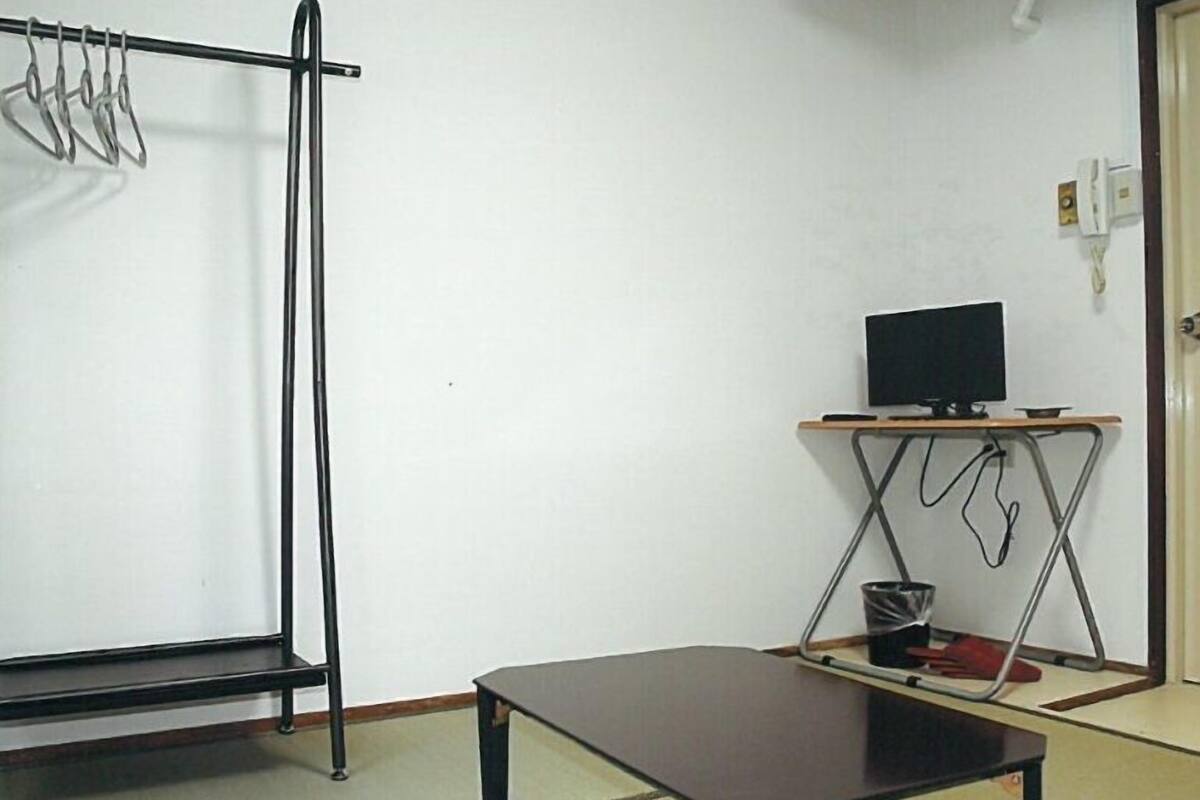 A room with a bed, a small table, a television on a stand, and a coat rack.