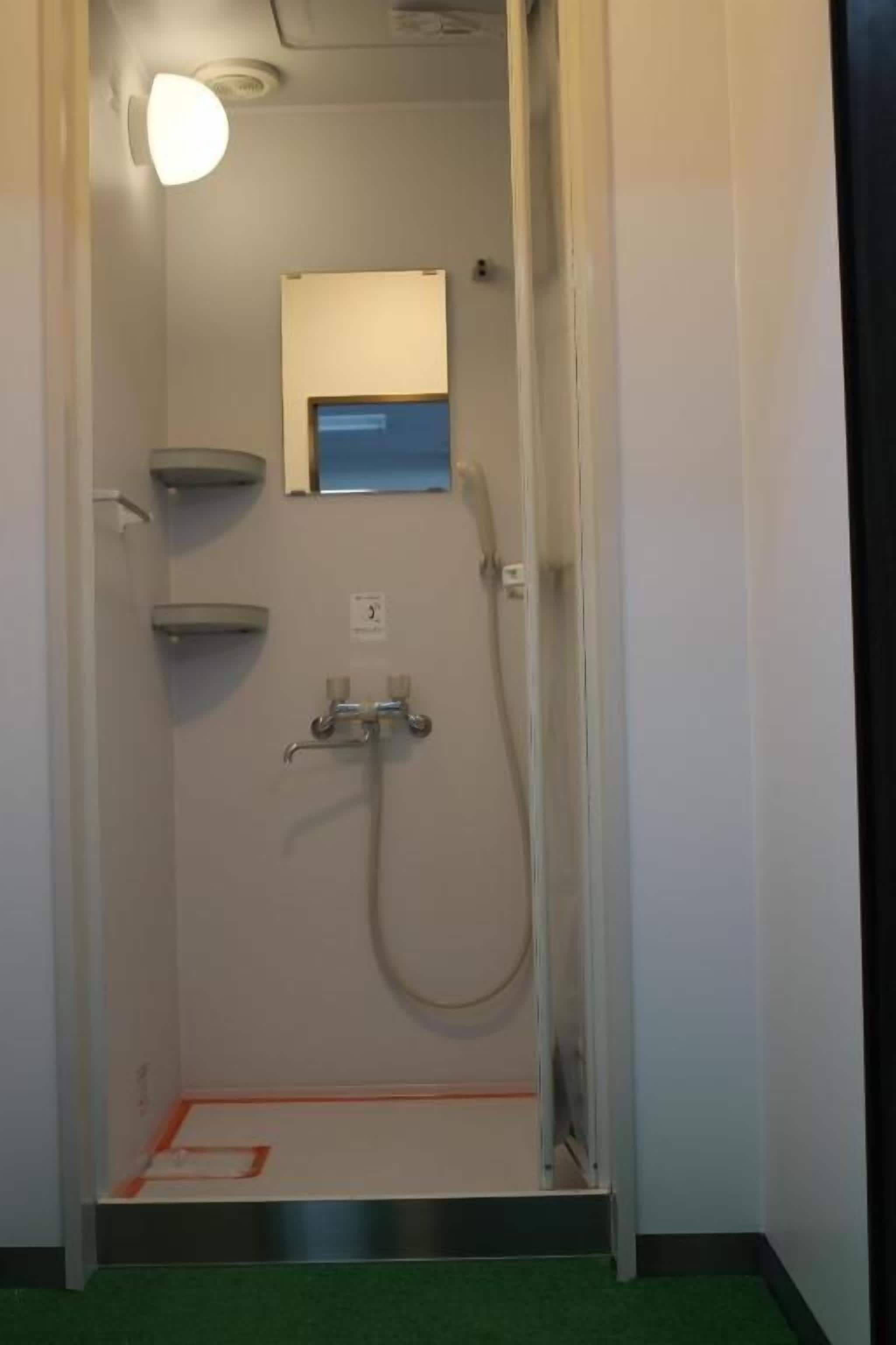 A small, enclosed shower area with a handheld showerhead, a wall-mounted mirror, and a step leading into the shower.